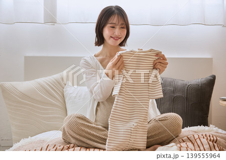 ベッドの上でベビー服を手に持ち微笑む若い女性 ベッドの上でベビー服を手に持ち微笑む若い女性 139555964