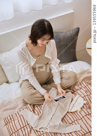 ベッドでエコー写真を見つめる妊婦とベビー服 ベッドでエコー写真を見つめる妊婦とベビー服 139555968