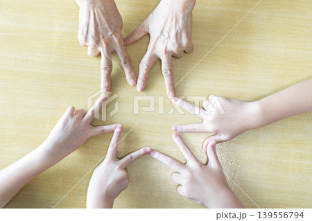 Children and an elderly woman point their fingers together to form a star, combining playful hand coordination with family unity and multigeneration teamwork. Children and an elderly woman point their fingers together to form a star, combining playful hand coordination with family unity and multigeneration teamwork. 139556794