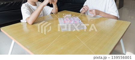 Two children pick colorful beads from a plastic organizer box on a wooden table. Elastic string and sorted beads in pastel and bright colors fill the divided compartments. 139556801