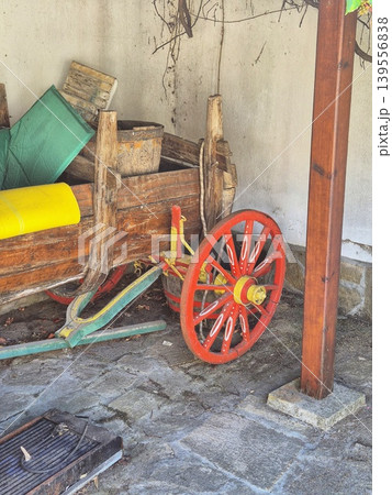 An old, rustic wooden cart with a red wheel filled with various items. An old, rustic wooden cart with a red wheel filled with various items. 139556838