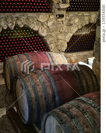 A place for wooden barrels for aging wine, in the background rows of wine bottles neatly laid out in niches in a stone wall. wine cellar. a place for storing and maturing wines. A place for wooden barrels for aging wine, in the background rows of wine bottles neatly laid out in niches in a stone wall. wine cellar. a place for storing and maturing wines. 139556880