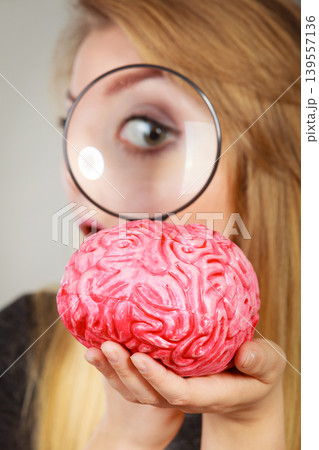 Woman holding magnifying glass investigating brain Woman holding magnifying glass investigating brain 139557136