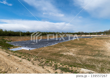 Workers prepare land for a new landfill. A black liner covers the area as equipment is set up. The site is located in a rural setting 139557267