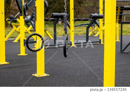 Workout rings hang from bright yellow poles in a fitness area where people can exercise. The field is surrounded by grass and trees Workout rings hang from bright yellow poles in a fitness area where people can exercise. The field is surrounded by grass and trees 139557295