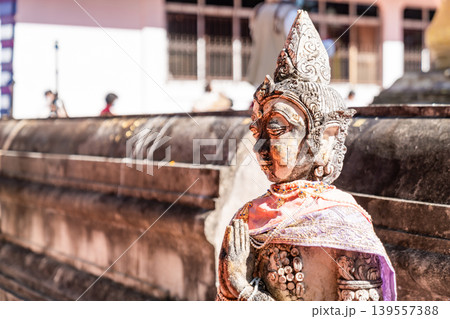 Weathered female guardian figure stands within a sacred temple site surrounded by historic stone structures and cultural heritage architecture. 139557388