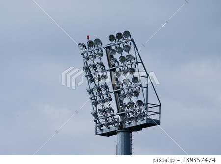 High stadium lighting mast with powerful floodlights against a cloudy sky. High stadium lighting mast with powerful floodlights against a cloudy sky. 139557474