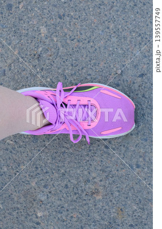 Foot in a purple sneaker with pink accents on gray asphalt. Sports footwear and a sporty lifestyle concept. 139557749