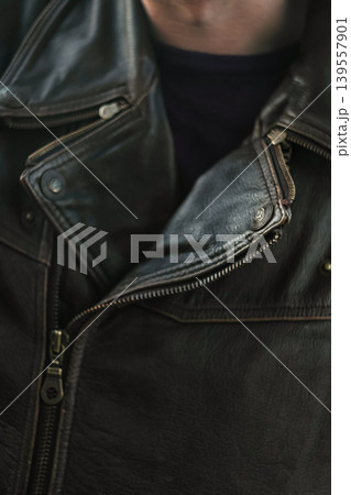 Close-up of a black leather biker jacket with zippers and metal buttons. Detail of a textured leather jacket worn by a man, focusing on the collar and metallic hardware Close-up of a black leather biker jacket with zippers and metal buttons. Detail of a textured leather jacket worn by a man, focusing on the collar and metallic hardware 139557901