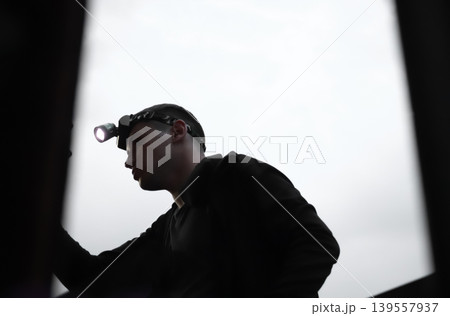 Silhouette of a young man with a headlamp performing a technical inspection or repair. professional lighting equipment. Concept blackout. Ukraine 139557937