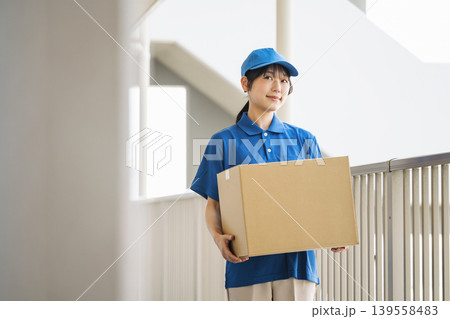 マンションに荷物を運ぶ配送業者の若い女性 マンションに荷物を運ぶ配送業者の若い女性 139558483