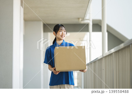 マンションに荷物を運ぶ宅配業者の若い女性 マンションに荷物を運ぶ宅配業者の若い女性 139558488