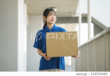 マンションに荷物を運ぶ宅配業者の若い女性 マンションに荷物を運ぶ宅配業者の若い女性 139558489