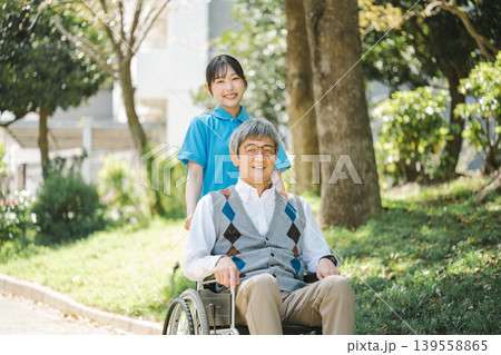 車椅子で公園を散策する若い介護士とシニア男性 139558865