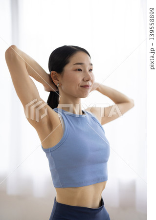 明るい窓辺で髪を結ぶヨガウェアを着た日本人のミドル女性 明るい窓辺で髪を結ぶヨガウェアを着た日本人のミドル女性 139558899