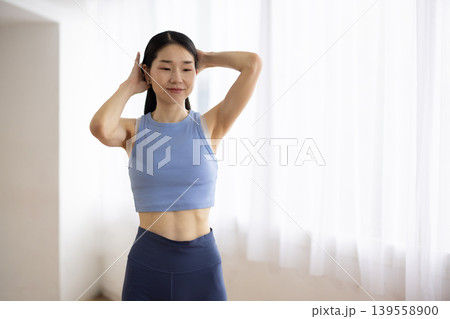 明るい窓辺で髪を結ぶヨガウェアを着た日本人のミドル女性 明るい窓辺で髪を結ぶヨガウェアを着た日本人のミドル女性 139558900