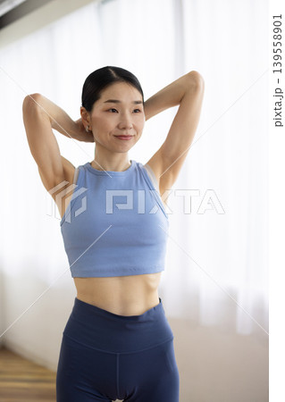 明るい窓辺で髪を結ぶヨガウェアを着た日本人のミドル女性 明るい窓辺で髪を結ぶヨガウェアを着た日本人のミドル女性 139558901