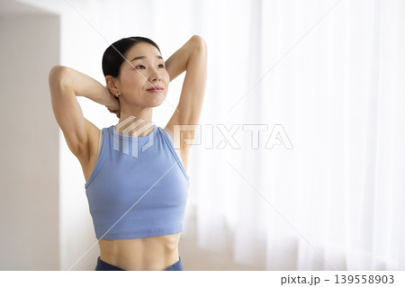 明るい窓辺で髪を結ぶヨガウェアを着た日本人のミドル女性 明るい窓辺で髪を結ぶヨガウェアを着た日本人のミドル女性 139558903