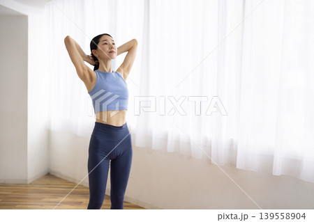 明るい窓辺で髪を結ぶヨガウェアを着た日本人のミドル女性 明るい窓辺で髪を結ぶヨガウェアを着た日本人のミドル女性 139558904