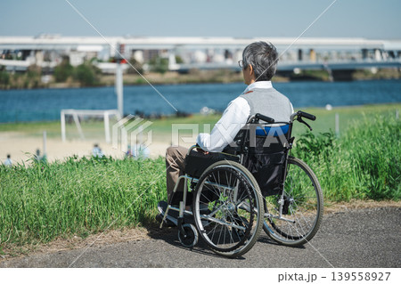 土手でのんびり過ごす車椅子に乗ったシニア男性 土手でのんびり過ごす車椅子に乗ったシニア男性 139558927