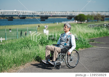 土手でのんびり過ごす車椅子に乗ったシニア男性 土手でのんびり過ごす車椅子に乗ったシニア男性 139558929