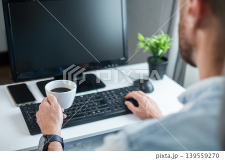 Man drinking coffee while working at computer desk 139559270