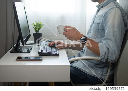 Man drinking coffee while working at computer desk 139559271