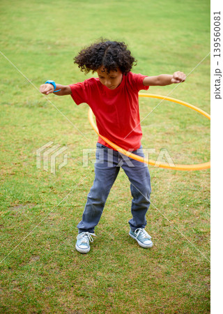 Child, playing and hula hoop on field on holiday, green grass and sunshine with energy in city. Young boy, mexican and game on playground, summer break and leisure with wellness in urban town Child, playing and hula hoop on field on holiday, green grass and sunshine with energy in city. Young boy, mexican and game on playground, summer break and leisure with wellness in urban town 139560081
