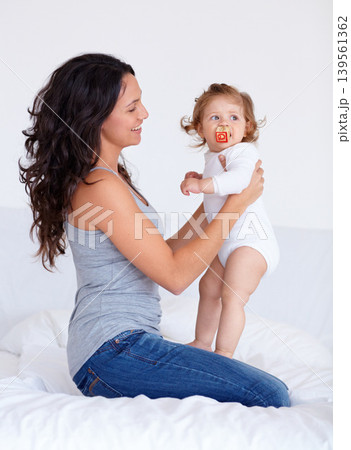 Bonding, sweet and mother playing with baby on bed in morning together at family home. Happy, smile and young mom having fun with girl infant, kid or toddler for child development in bedroom at house Bonding, sweet and mother playing with baby on bed in morning together at family home. Happy, smile and young mom having fun with girl infant, kid or toddler for child development in bedroom at house 139561362