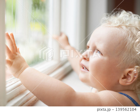 Baby, window and child thinking by glass at home, curious and sad alone. Young kid, blonde toddler and dream of cute girl at house, watching and childhood expression of learning with rain weather Baby, window and child thinking by glass at home, curious and sad alone. Young kid, blonde toddler and dream of cute girl at house, watching and childhood expression of learning with rain weather 139562104