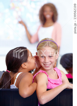 Little girls, whisper and classroom in ear for secret, gossip or communication in lesson at school. Children, students or friends listening to rumor, information or class together with teacher 139562109