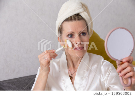 Woman applying facial treatment while looking into a mirror at home in a serene setting Woman applying facial treatment while looking into a mirror at home in a serene setting 139563002