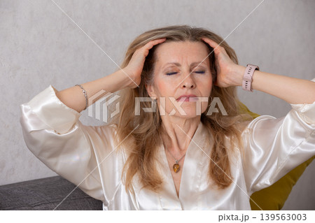 Woman in a silk blouse relaxing at home while managing stress in a cozy living room with neutral colors 139563003