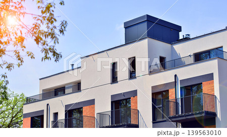 Architecture and real estate, residential apartment building with large panoramic windows. Modern building surrounded by nature, park, green trees, and blue sky background. Architecture and real estate, residential apartment building with large panoramic windows. Modern building surrounded by nature, park, green trees, and blue sky background. 139563010