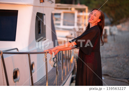 Smiling woman enjoying sunset by the marina while leaning on the boat railing Smiling woman enjoying sunset by the marina while leaning on the boat railing 139563227