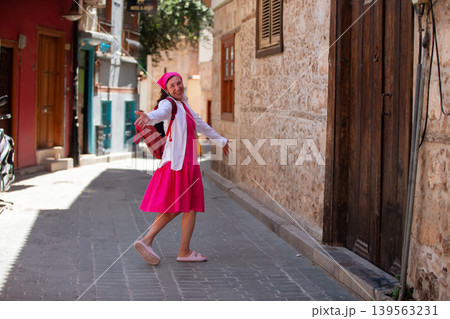 An adult woman in a pink dress is happy to explore the charming cobblestone lane in a historical city on a sunny day An adult woman in a pink dress is happy to explore the charming cobblestone lane in a historical city on a sunny day 139563231