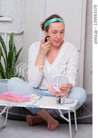 Woman applying skincare product while sitting on floor in cozy indoor setting during daytime 139563379