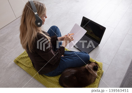 Woman studies with laptop and cat on a cozy mat in a modern home office Woman studies with laptop and cat on a cozy mat in a modern home office 139563451