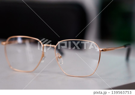 Close up of stylish gold eyeglasses resting on white surface with blurred black background for fashion accessory concept 139563753