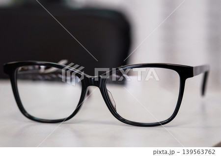 Black Eyeglasses Sitting On White Surface With Blurred Background For Vision And Optometry Concepts Black Eyeglasses Sitting On White Surface With Blurred Background For Vision And Optometry Concepts 139563762