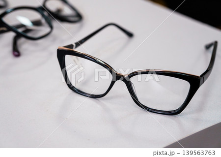Selective focus on black eyeglasses with gold accents resting on white surface, shallow depth of field, minimalist stock photo 139563763
