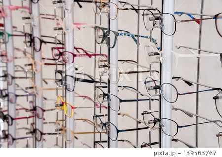 Collection of eyeglasses frames hanging on white display rack in optical shop interior with variety of styles and colors for vision care retail Collection of eyeglasses frames hanging on white display rack in optical shop interior with variety of styles and colors for vision care retail 139563767
