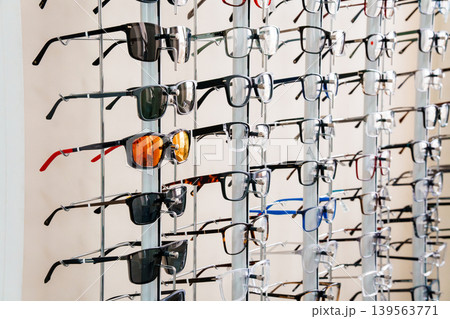 Display of eyeglasses and sunglasses for sale at optical store with colorful frames on metal rack 139563771