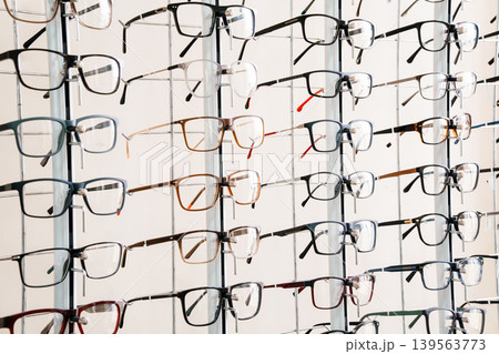 Multiple pairs of eyeglasses displayed on a white rack for sale at an optical shop with colorful frames 139563773