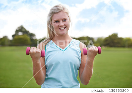 Woman, portrait and dumbbells outdoor for exercise with smile for workout, training or fitness on sports field. Athlete, person and happy for physical activity or blue sky on grass with equipment 139563809