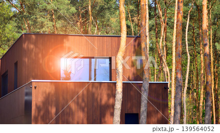 Villa surrounded by trees on bright sunny day. Beautiful exterior of modern luxury home with linear design and elegant use of wood and metal. Villa surrounded by trees on bright sunny day. Beautiful exterior of modern luxury home with linear design and elegant use of wood and metal. 139564052