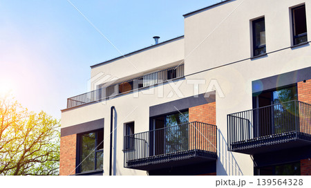 Architecture and real estate, residential apartment building with large panoramic windows. Modern building surrounded by nature, park, green trees, and blue sky background. Architecture and real estate, residential apartment building with large panoramic windows. Modern building surrounded by nature, park, green trees, and blue sky background. 139564328