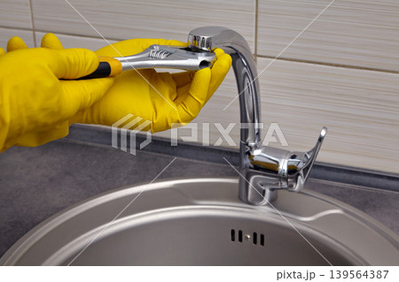 repairing a kitchen sink faucet with gloves and a wrench repairing a kitchen sink faucet with gloves and a wrench 139564387