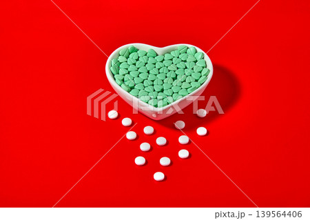 turquoise heart-shaped cardiology pills in a ceramic bowl on a red background. turquoise heart-shaped cardiology pills in a ceramic bowl on a red background. 139564406