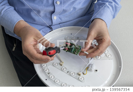 Technician maintaining, repairing or assembling of an LED ceiling light, commonly referred to as an oyster light fixture Technician maintaining, repairing or assembling of an LED ceiling light, commonly referred to as an oyster light fixture 139567354